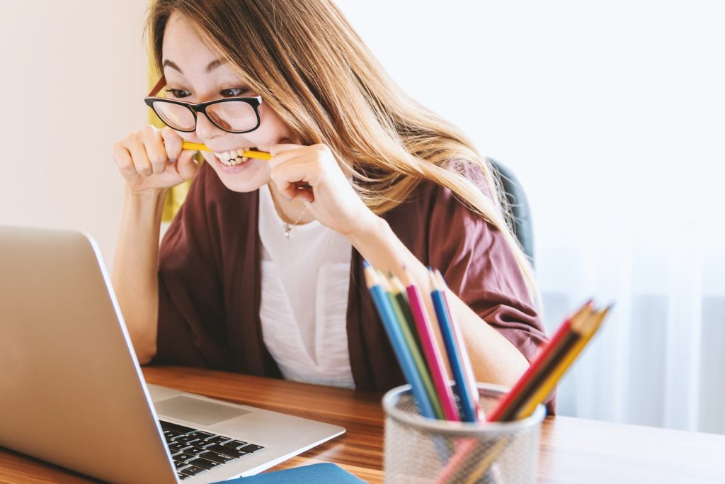 laptop buying guide - woman biting pencil while sitting on chair in front of computer